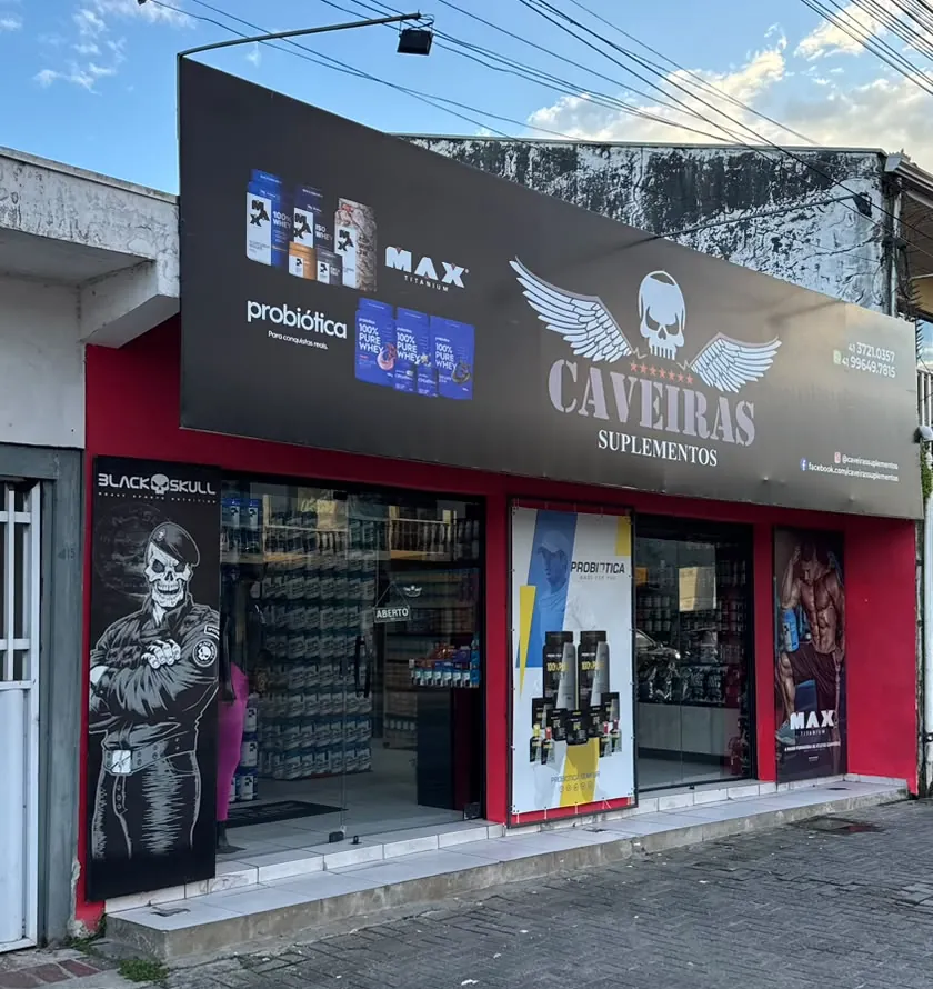 Fachada da Caveiras Suplementos em Paranaguá: placa preta com o logo da loja e parede vermelha