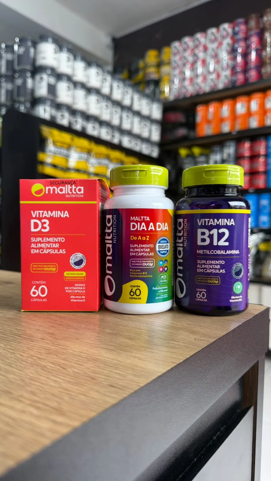 Caixa de vitamina D3, frasco do polivitamínico Dia a Dia e frasco de vitamina B12 da Maltta, no balcão da loja