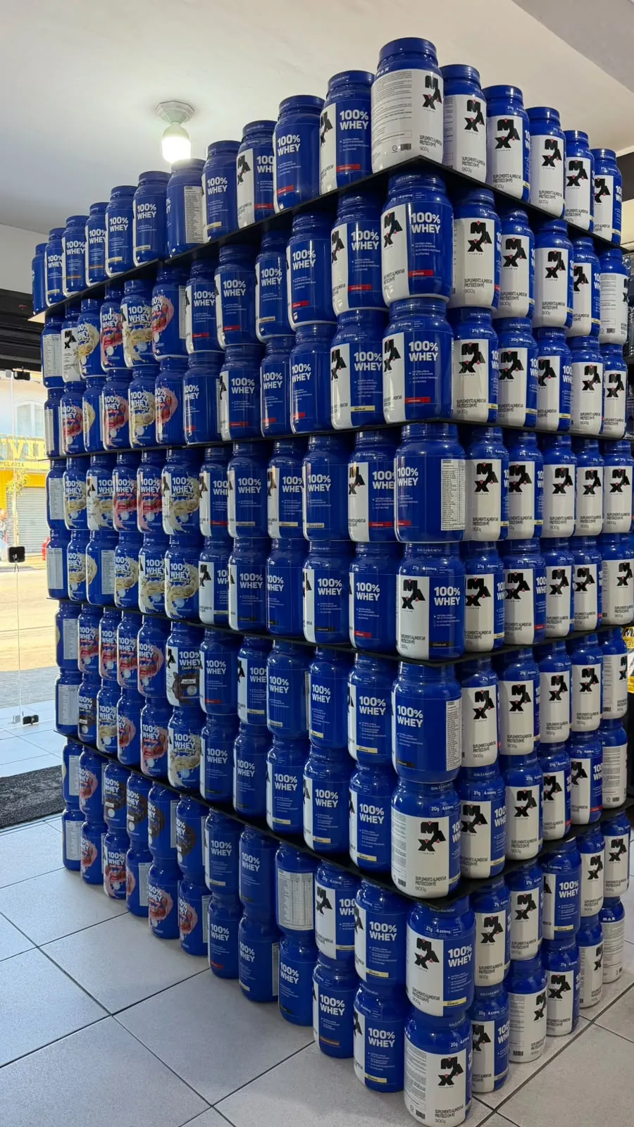 Parede de potes de 100% Whey da Max Titanium, do chão ao teto, dentro da loja